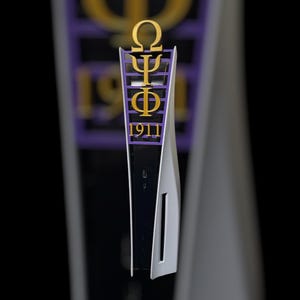 以下が含まれることがあります： 白と黒のゲーム機に、紫と金のカスタムアクセントピースが付いています。アクセントピースには、ギリシャ文字のオメガ、プサイ、ファイと数字の1911が描かれています。ゲーム機は黒い背景に配置されています。