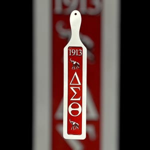 May include: A white wooden paddle with a red background. The paddle has the Greek letters Delta, Sigma, and Theta, along with the year 1913 and an elephant image.