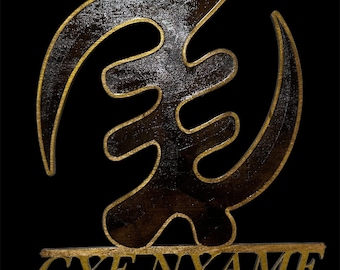 May include: A wooden wall hanging with a gold outline of the Adinkra symbol Gyenyame, which represents strength and power. The symbol is on a black background with the word "GYENYAME" written in gold below it.