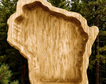May include: A wooden decorative tray in the shape of the state of Wisconsin. The tray is light brown with a textured surface and a carved-out interior. The background features a forest of tall green pine trees.