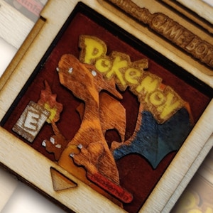 Peut inclure: Une découpe en bois d'une cartouche de jeu Game Boy avec un design Pokemon. La cartouche est brune avec un logo Pokemon rouge et jaune. Le texte "Game Boy" est imprimé sur le dessus de la cartouche. L'image est un fichier numérique uniquement et est prête pour la découpe CNC.