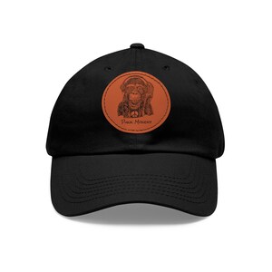 May include: Black baseball cap featuring a circular patch with a monkey wearing headphones and a peace sign. The patch is brown with the words "Punk Monkey" in a script font. The cap has a curved brim.