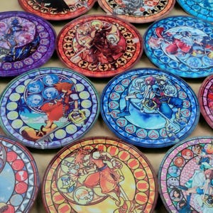 Puede incluir: Una colección de posavasos redondos y coloridos con ilustraciones de estilo vidriera. Cada posavasos muestra diferentes personajes y escenas, con tonos vibrantes de rojo, azul, morado y amarillo. Los posavasos están dispuestos en un patrón de cuadrícula.