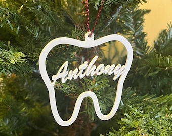May include: White tooth-shaped Christmas ornament with the name "Anthony" written in a cursive font.