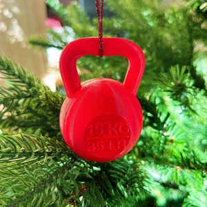 Könnte beinhalten: Roter Weihnachtsbaumschmuck in Form einer Kettlebell mit dem Text "15 KG 35 LB" darauf.