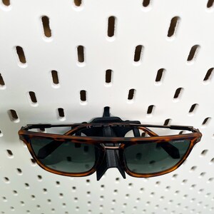 May include: Brown tortoise shell sunglasses with black frames and a black plastic hook for hanging on a pegboard.