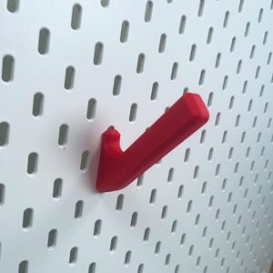 K&ouml;nnte beinhalten: Ein roter Plastikhaken, der zum Aufh&auml;ngen an einer Lochwand gedacht ist.