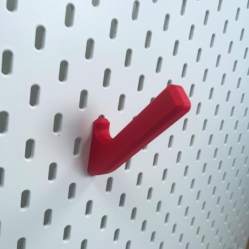 K&ouml;nnte beinhalten: Ein roter Plastikhaken, der zum Aufh&auml;ngen an einer Lochwand gedacht ist.