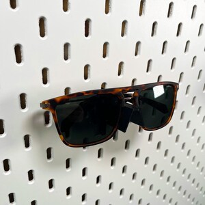May include: Tortoise shell sunglasses with brown lenses. The sunglasses are hanging on a white pegboard.