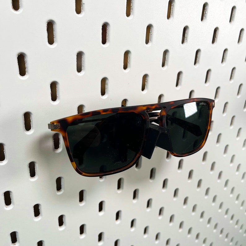May include: Tortoise shell sunglasses with brown lenses. The sunglasses are hanging on a white pegboard.