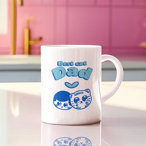 Op de afbeelding: Witte keramische mok met een blauw ontwerp waarop "Best cat Dad" staat met een hartje en twee cartoongezichten, een van een kat en een van een persoon. De mok staat op een wit aanrecht.