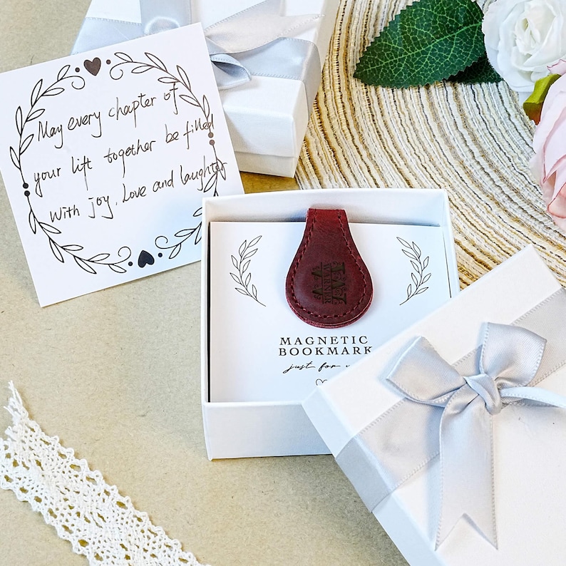 Pu&ograve; includere: Un segnalibro magnetico in pelle rossa all'interno di una confezione regalo bianca. Il segnalibro presenta un design in rilievo. &Egrave; visibile anche una carta con il testo "May every chapter of your life together be filled with joy. Love and laughter".
