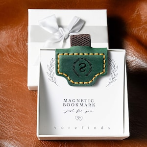May include: A green leather magnetic bookmark with the number 2 inside a laurel wreath design. The bookmark has yellow stitching and a brown fabric tab. The packaging includes the text "MAGNETIC BOOKMARK" and "just for you."