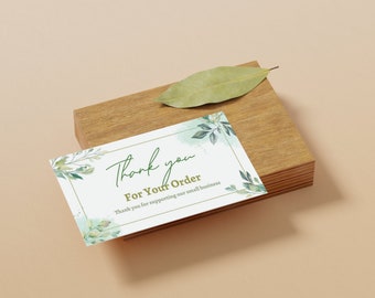 May include: A white card with the words "Thank you For Your Order" in green script, accented with watercolor-style green leaves and a gold border. The card rests on a small wooden block with a dried leaf on top.