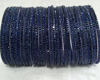 May include: A stack of blue bangle bracelets with a sparkly finish. The bracelets are made of glass or plastic and are decorated with small, shiny stones.