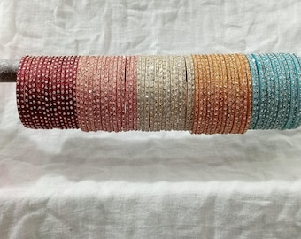 May include: A set of colorful bangles with rhinestones. The bangles are arranged in a row and are made of a shiny material. The bangles are in shades of red, pink, white, gold, and blue.
