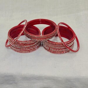May include: A set of red bangles with clear rhinestones. The bangles are stacked on top of each other.