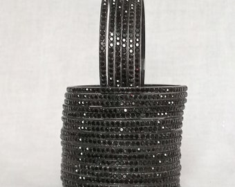 May include: A stack of black bangles with small black rhinestones. The bangles are arranged in a circle.