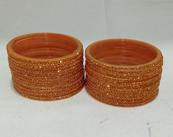 May include: A set of orange glass bangles with a sparkly finish. The bangles are stacked together in two piles.