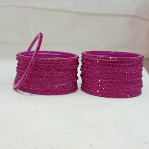 May include: A set of pink bangles with sparkly accents. The bangles are stacked in two piles, with one pile slightly higher than the other.