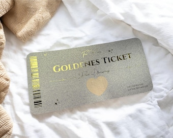 Puede incluir: Una tarjeta rectangular plateada con letras doradas que dicen "GOLDENES TICKET" y otro texto. Un corazón dorado está en el centro. Un código de barras está en el lado izquierdo. La tarjeta está sobre una superficie blanca.