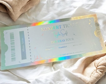 Puede incluir: Una entrada de concierto rectangular con acabado holográfico que muestra el texto KONZERT TICKET, Taylor Swift, THE ERAS TOUR, Frankfurt, 21.04.2025 y Allianz Arena. La entrada incluye un código de barras, estrellas pequeñas y una nota musical.