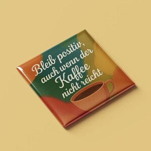 Könnte beinhalten: Ein bunter quadratischer Knopf mit dem Text "Bleib positiv, auch wenn der Kaffee nicht reicht" und einer stilisierten Illustration einer Tasse Kaffee.