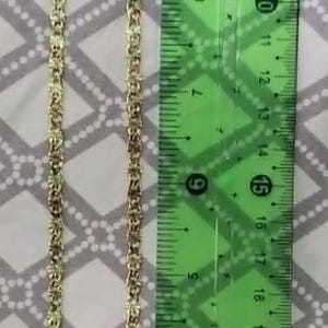 May include: A gold-colored chain necklace with a repeating pattern of rectangular links. The necklace is approximately 29 cm long, as measured by a green ruler with the brand name "Jocar".