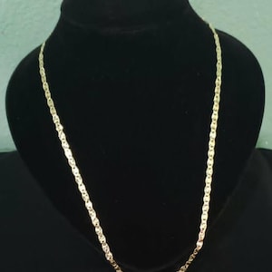May include: A gold-colored chain necklace with a twisted link design. The necklace is displayed on a black mannequin bust. The chain has a shiny finish and is suitable for everyday wear or special occasions.