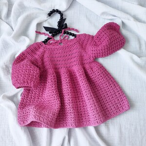 May include: A pink crocheted baby dress with puffed sleeves