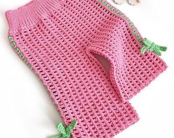 Puede incluir: Pantalones de crochet rosa con ribetes y lazos verdes en las piernas.