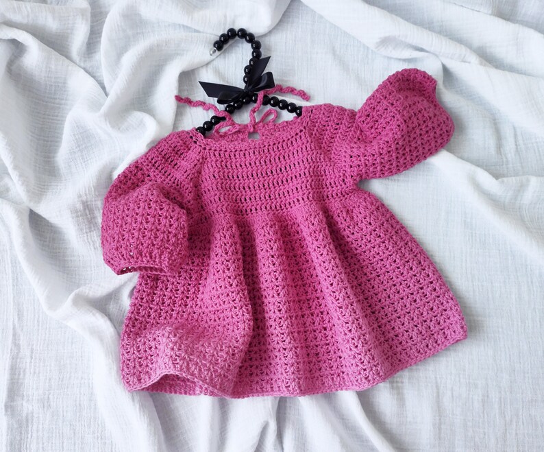 May include: A pink crocheted baby dress with puffed sleeves