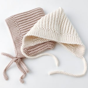 Könnte beinhalten: Zwei gestrickte Baby-Mützen, eine in hellrosa und die andere in cremefarben, mit Bändern.