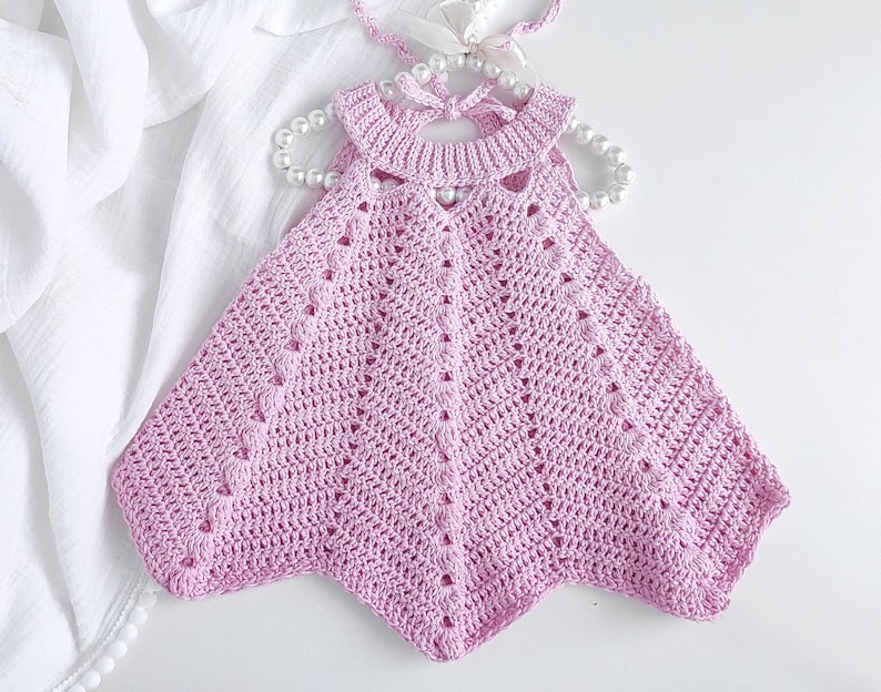 May include: A pink crocheted baby dress with a scalloped hem and a delicate openwork design.