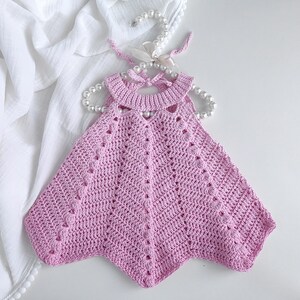 May include: A pink crocheted baby dress with a scalloped neckline and a delicate, openwork design.