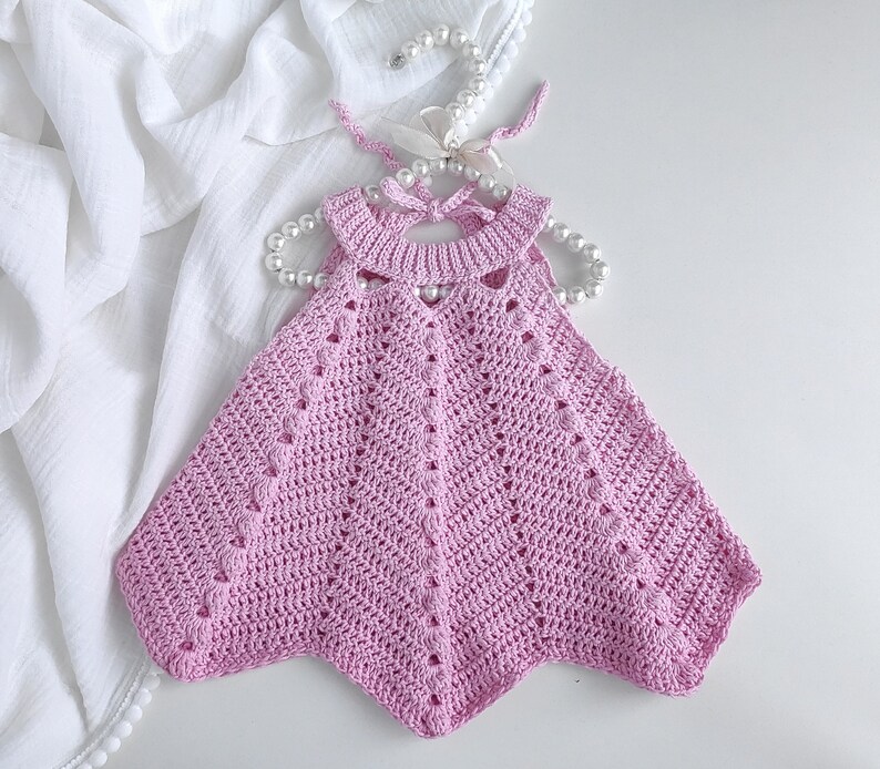 May include: A pink crocheted baby dress with a scalloped neckline and a delicate, openwork design.