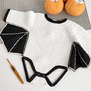 May include: White crocheted baby onesie with black crocheted bat wings and trim.
