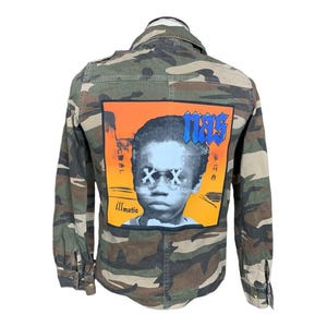 May include: Camouflage jacket with a graphic on the back featuring a portrait of a young boy with the word "NAS" in blue block letters. The graphic also includes the word "illmatic".
