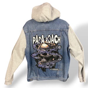 May include: A denim jacket with a grey hood and sleeves. The back of the jacket features a skull graphic wrapped in chains, with the band name "PAPA ROACH" above it. The jacket has a button-up front and two chest pockets.