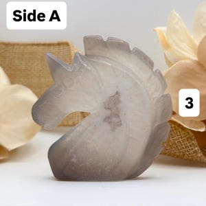May include: A carved, gray and white unicorn head figurine. The sculpture is made of a translucent stone, with visible internal patterns. The text "Side A" is in the upper left corner, and the number "3" is in the upper right corner.