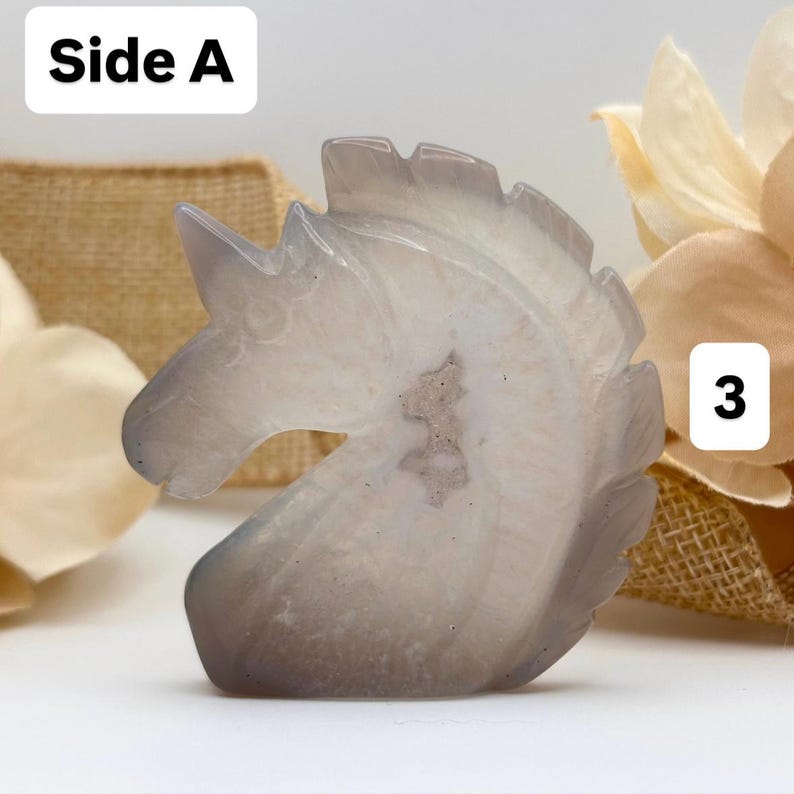 May include: A carved, gray and white unicorn head figurine. The sculpture is made of a translucent stone, with visible internal patterns. The text "Side A" is in the upper left corner, and the number "3" is in the upper right corner.