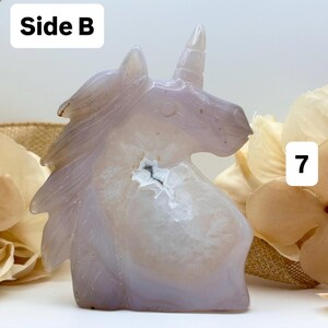 May include: A carved, light purple unicorn figurine. The crystal sculpture has a white and gray interior with a small cavity. The text "Side B" is in the upper left corner, and the number "7" is in the upper right corner.