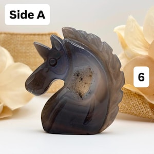 May include: A carved stone unicorn figurine in shades of gray and white. The sculpture is detailed with a horn, eye, and mane. The text "Side A" is in the upper left corner, and the number "6" is in the upper right corner.