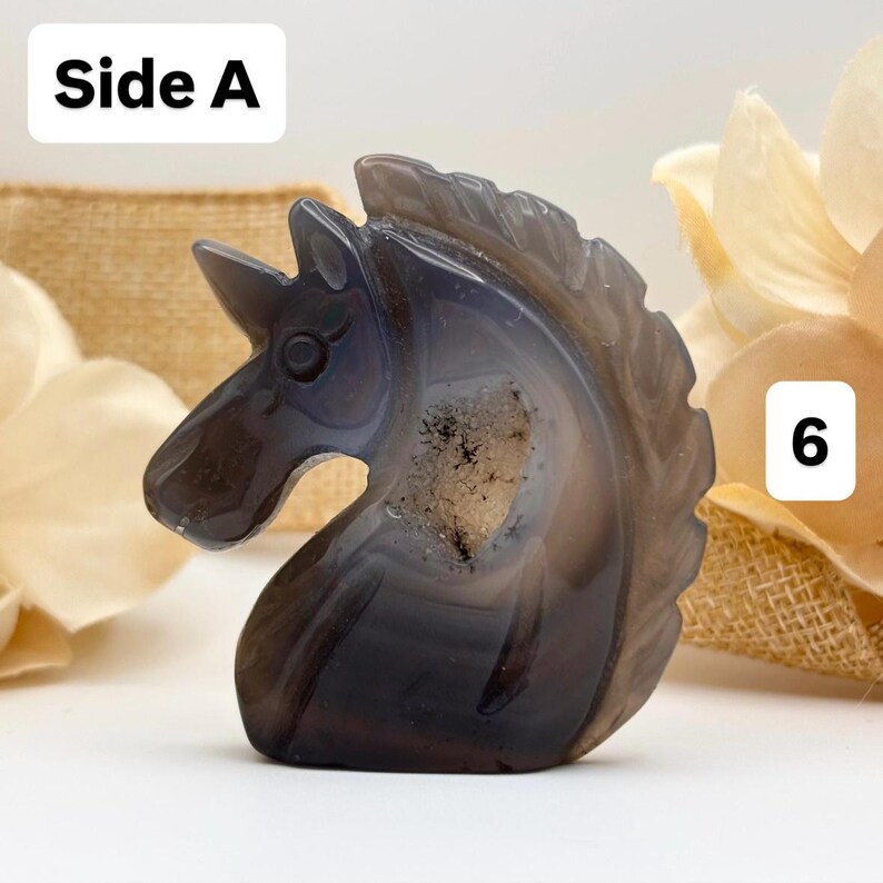 May include: A carved stone unicorn figurine in shades of gray and white. The sculpture is detailed with a horn, eye, and mane. The text "Side A" is in the upper left corner, and the number "6" is in the upper right corner.