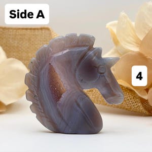 May include: A carved stone unicorn head in shades of gray and purple. The sculpture has a detailed mane, horn, and facial features. The text "Side A" is in the upper left corner, and the number "4" is in the upper right corner.
