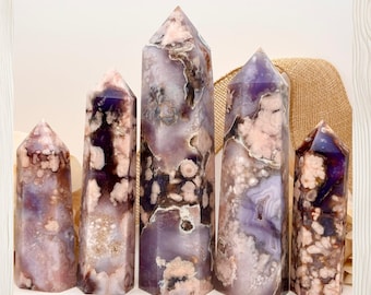 May include: Five polished crystal towers of varying heights, featuring a mix of translucent purple, lavender, and opaque white floral-like inclusions. The stones have a smooth, faceted surface with natural mineral patterns throughout.