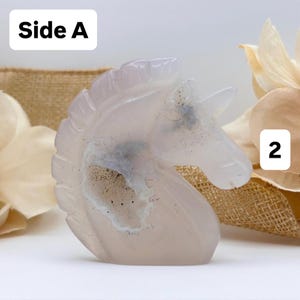 May include: A carved, translucent, light pink unicorn figurine. The sculpture has a detailed mane and horn. The text "Side A" is in a white box in the upper left corner, and the number "2" is in a white box in the upper right corner.