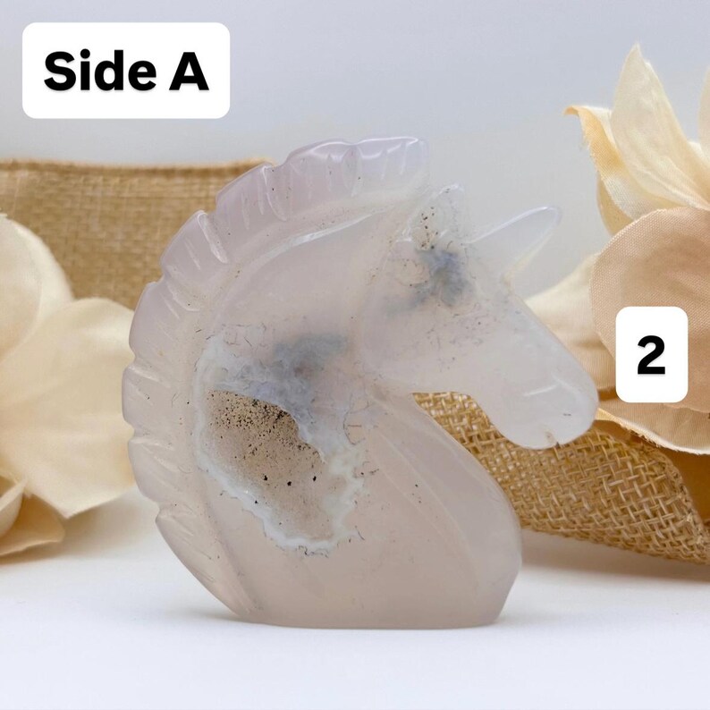 May include: A carved, translucent, light pink unicorn figurine. The sculpture has a detailed mane and horn. The text "Side A" is in a white box in the upper left corner, and the number "2" is in a white box in the upper right corner.