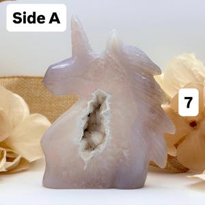 May include: A carved, light purple unicorn figurine with a geode center. The unicorn has a detailed mane and horn. The geode is white and brown. The text "Side A" and the number "7" are visible.