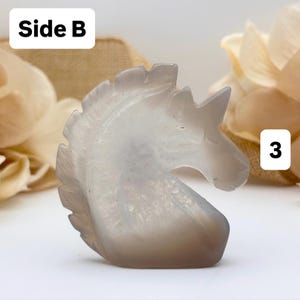May include: A carved, gray-toned unicorn figurine. The sculpture is detailed, with a flowing mane and a prominent horn. The text "Side B" is in a white box in the upper left corner, and the number "3" is in a white box in the lower right corner.